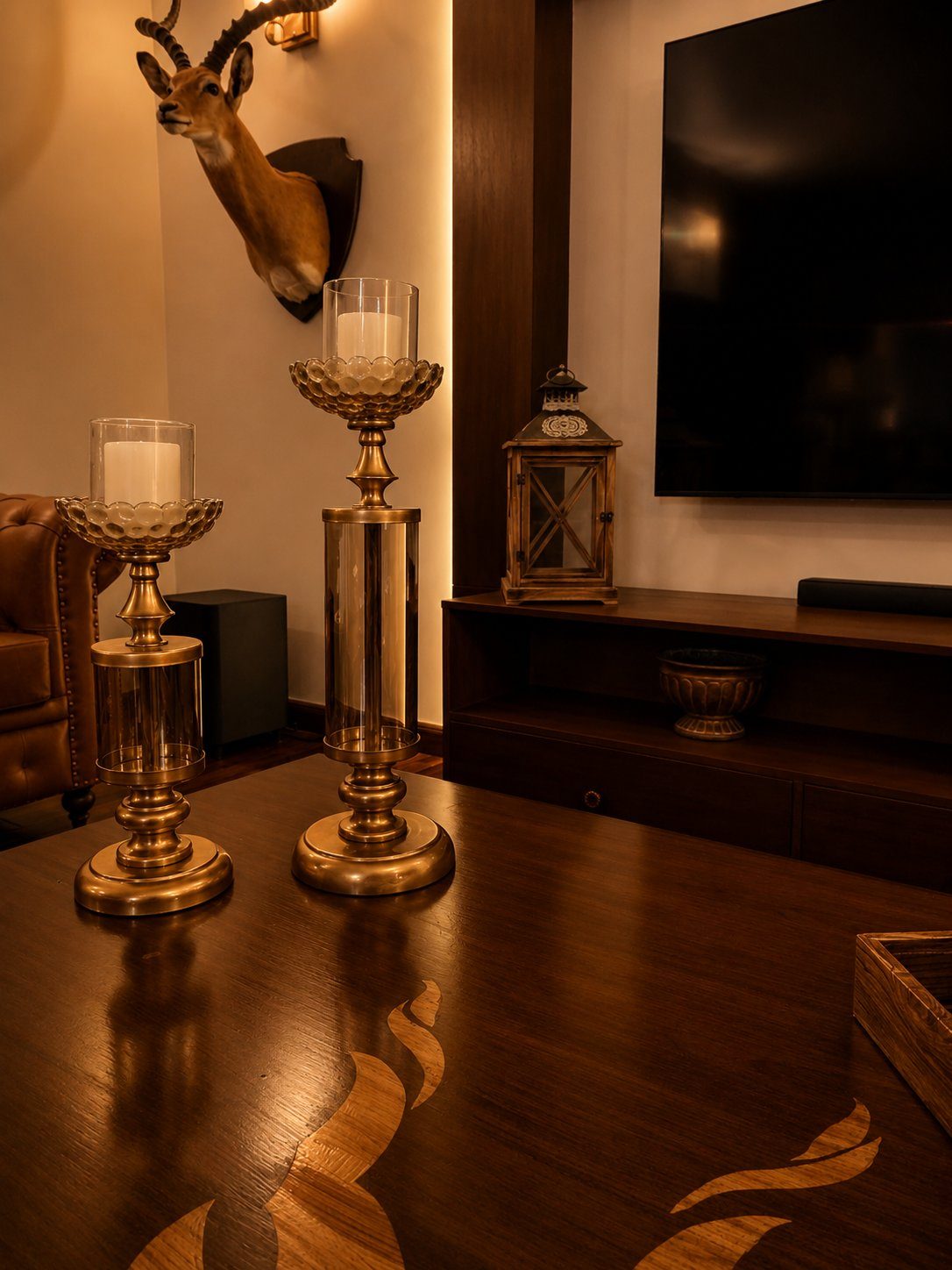 Brass candle holders on dark wood table beneath mounted gazelle head