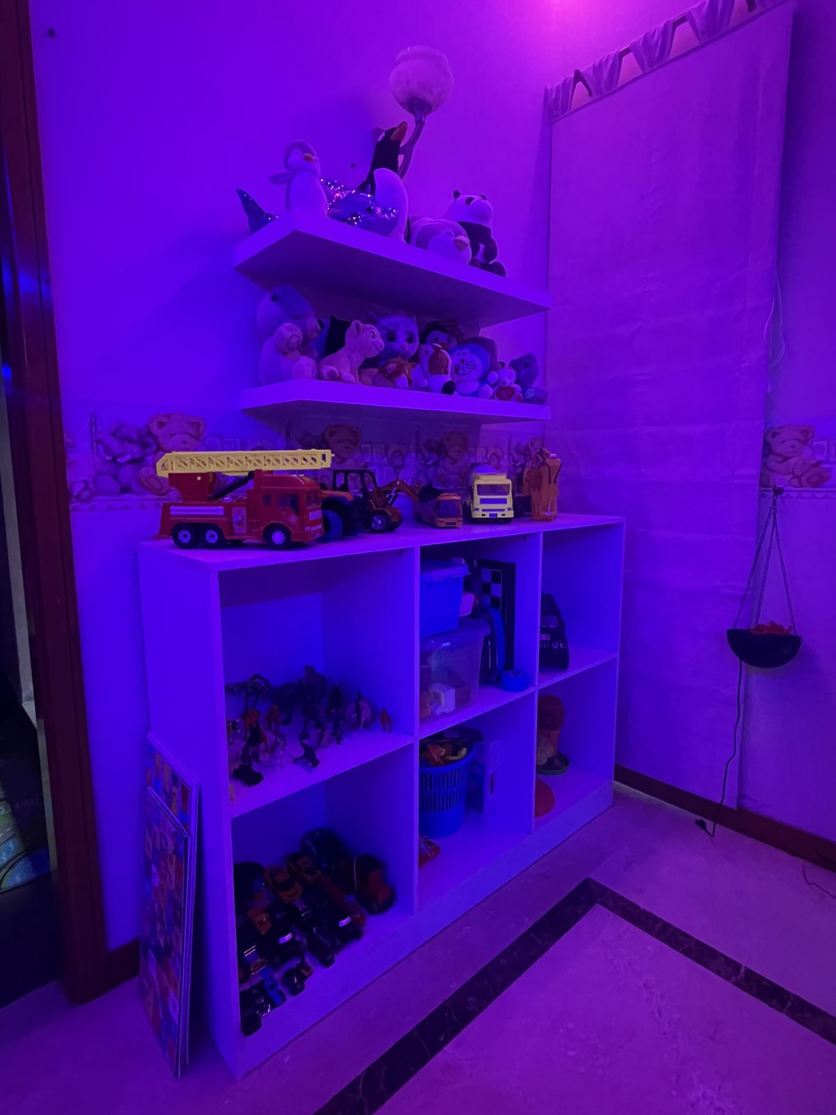 White shelving unit filled with toys under purple lighting