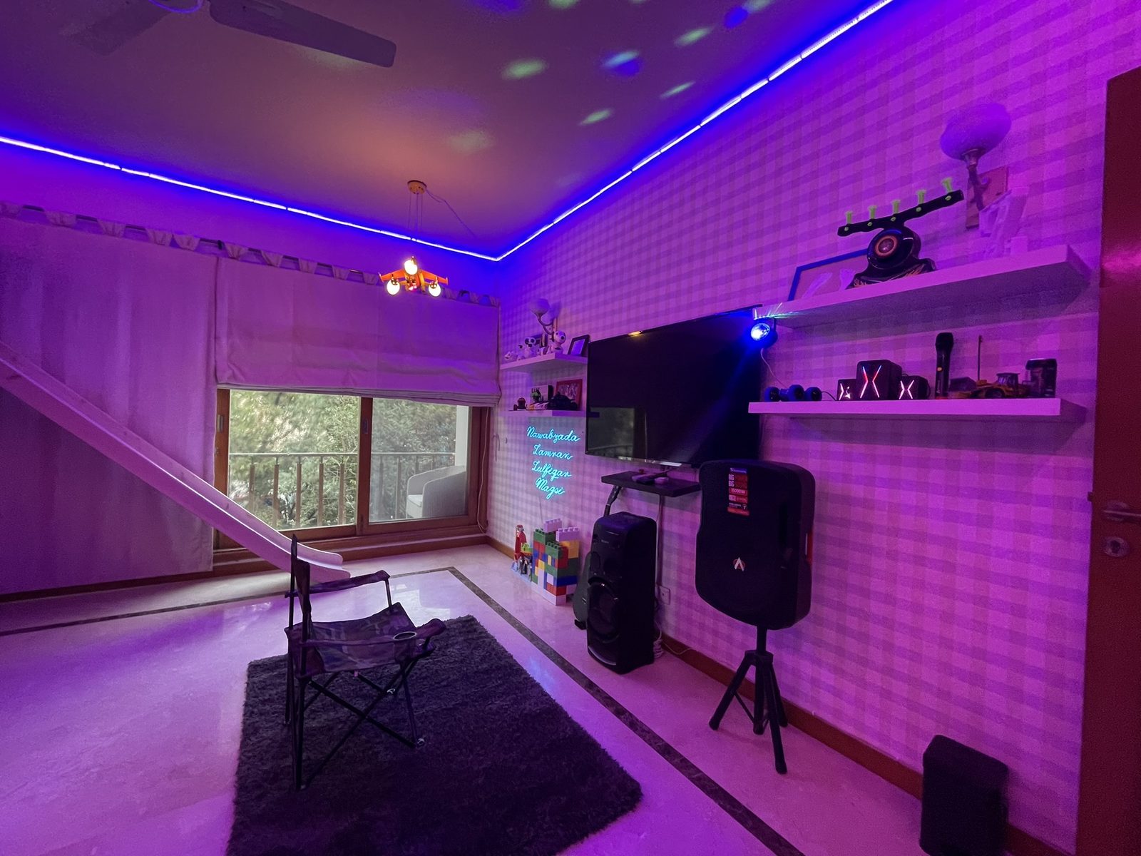 Purple-lit gaming corner with TV, speakers and neon name sign